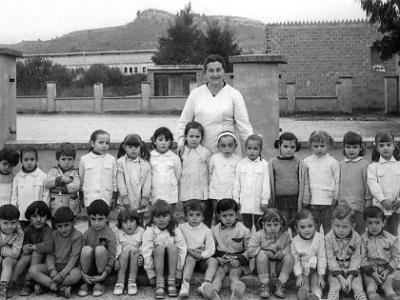 carmescola  (?), ANNA SIMÓ SALA, XAVIER FALCÓ SEGURA, MARI RAMIS JOVELLS, DOLORS COLUNGO, MARISA MARTÍ RIBELLES, DOLORS ROCA CURCÓ, ROSA MARIA MATEU DURAN, ISABEL BELLET ORONICH, NACI LLOVERA CARBONELL, MERCEDES EZQUERRA ESPÍN, RAMONA ARAGÜÉS I ÚRSULA REBULL PONS. SENTATS: JOAN CUADRAT RAMIS, PEPE COLCHERO GONZÁLEZ, LLORENÇ BARÓ CONTRERAS, JOAN FARRAN JOVÉ, (?), (?), ALFONS MATEU DURAN, JOSEP SEGURA FARRÚS, ISABEL EZQUERRA ESPÍN, MARIA JOVÉ BELLET, FREDERIC BARBERÀ FARRAN I FELIP BELLET LÓPEZ.  MESTRA MARIA REBULL.